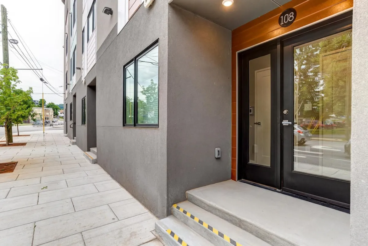 An exterior view of the main entrance door, a staircase leading up, detailed architecture of the building, and the surrounding sidewalk that hints at a welcoming, community-focused environment. The mood is inviting, and the perspective captures the initial arrival experience.