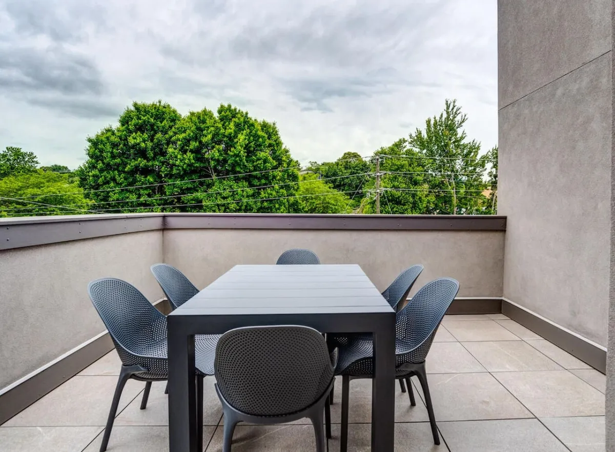 An outdoor dining area with a table and chairs set amidst greenery, evoking a private patio atmosphere. The space is ideal for enjoying meals, coffee, or evening drinks while taking in tranquil surroundings and fresh air.