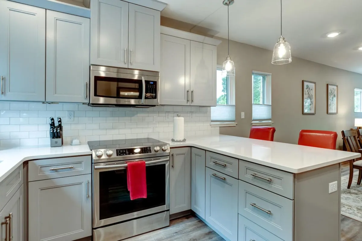 A modern kitchen featuring stainless steel appliances, a pristine white countertop, and vibrant red accents. The open space invites conversation and collaboration, whether cooking together or celebrating special occasions.
