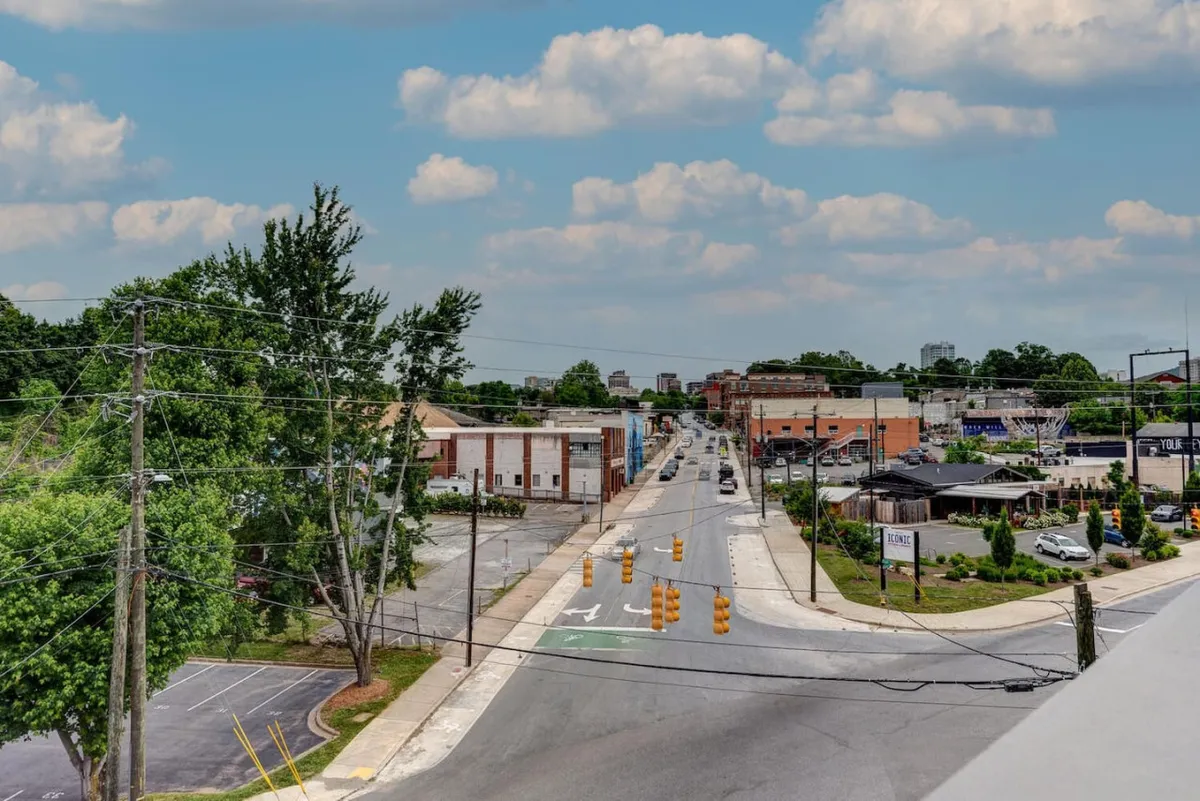 A tree-lined street in downtown Asheville, flanked by classic downtown buildings. Traffic signals and subtle foot traffic hint at the active, accessible nature of the area, perfect for exploring on foot.