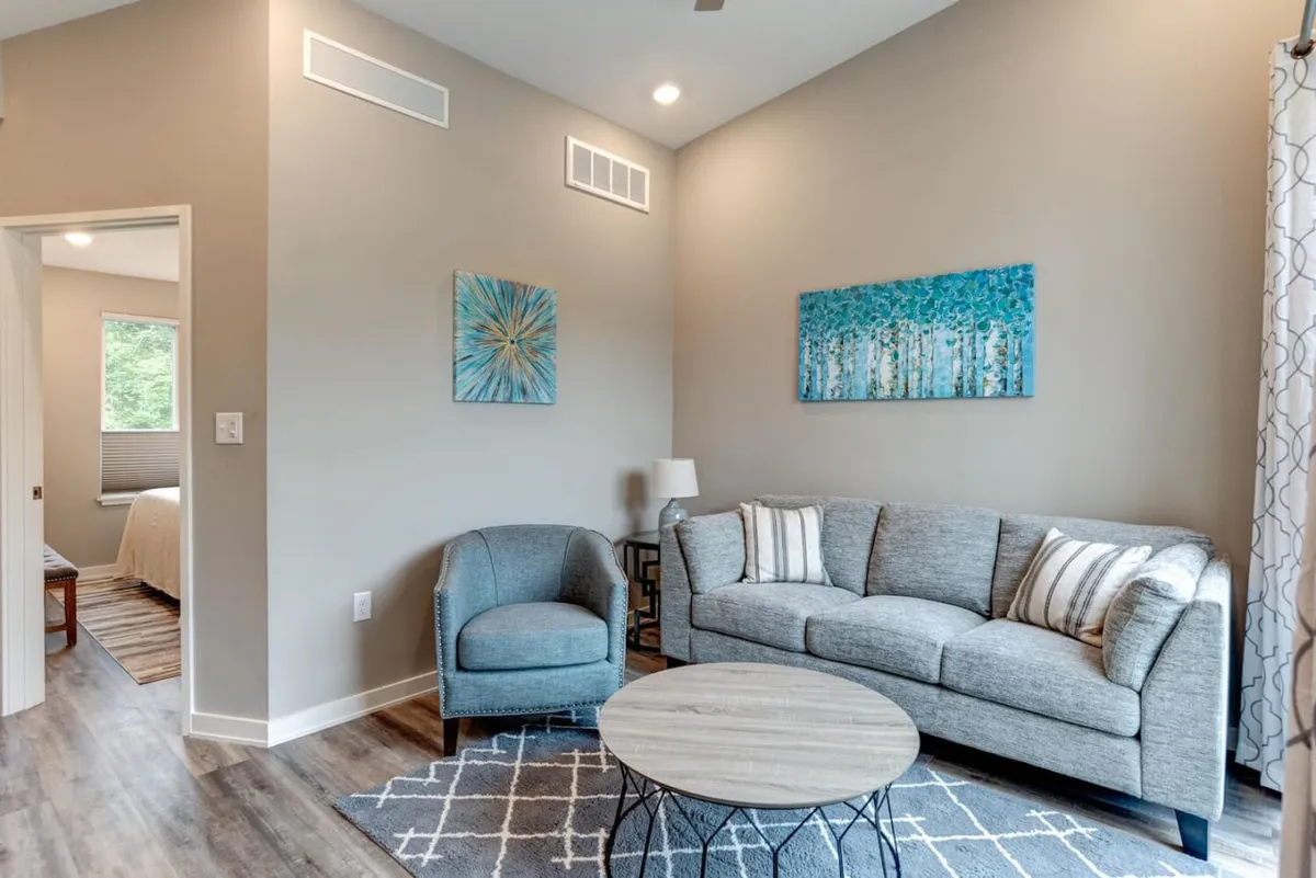 A comfortable living area featuring a cozy sofa, decorative artwork, a coffee table, and an inviting armchair. The space is arranged for relaxation and socializing, and the layout hints at openness and potential access to other parts of the home, possibly connecting to a patio or rooftop area.